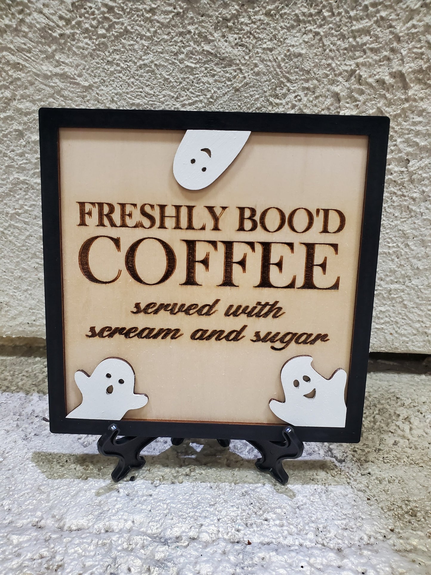 Decorative sign with 'Freshly Bood Coffee' text and ghost illustrations on a stand.