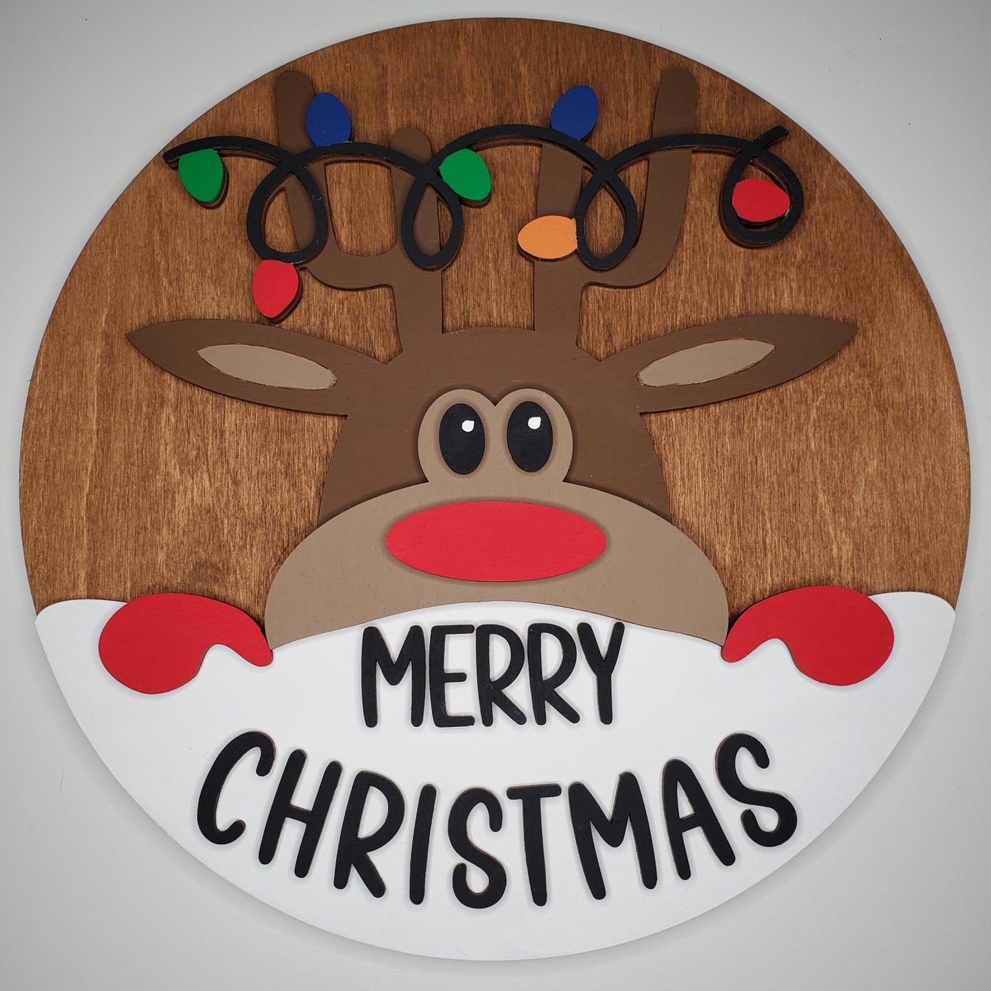 Wooden reindeer decoration with 'Merry Christmas' text and colorful lights on a plain background