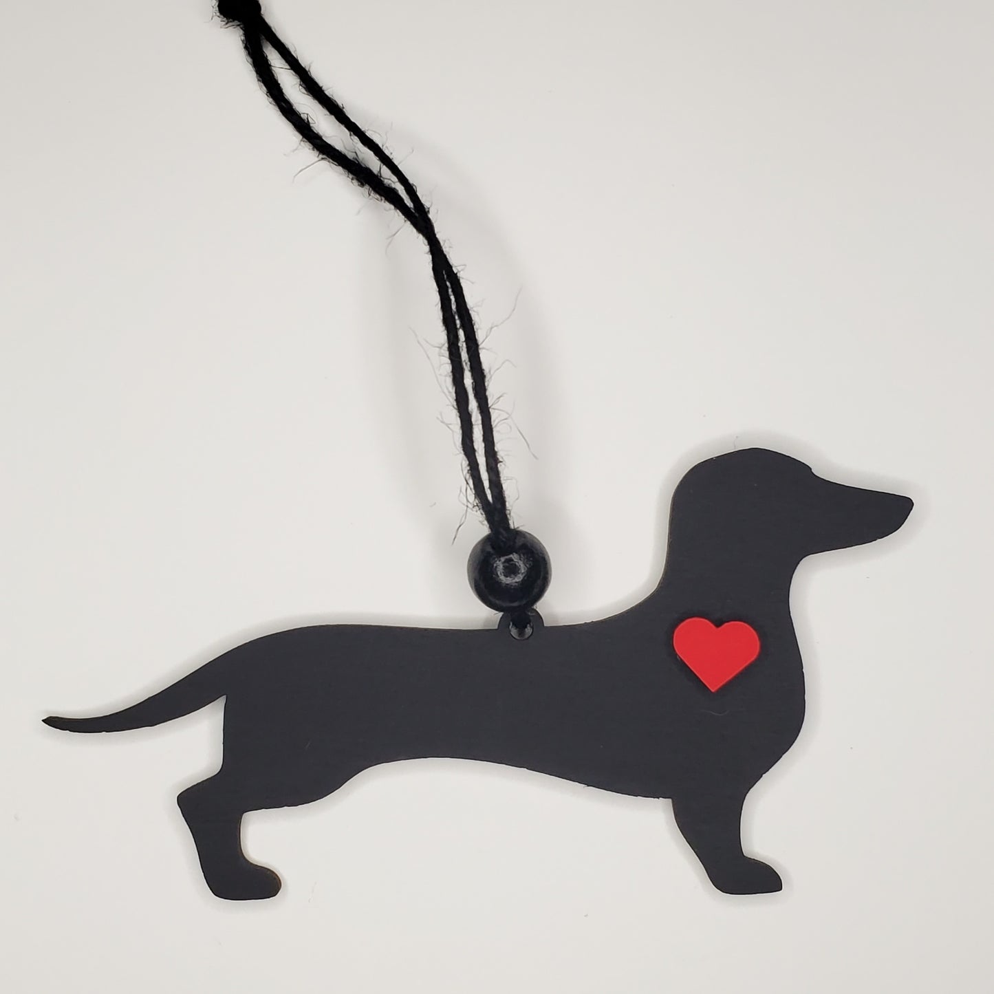 Black dachshund-shaped pendant with a red heart on a white background