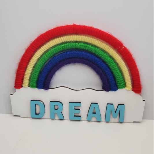 A laser cut wooden rainbow "Dream" decoration featuring colorful yarn as the rainbow. Hand Painted