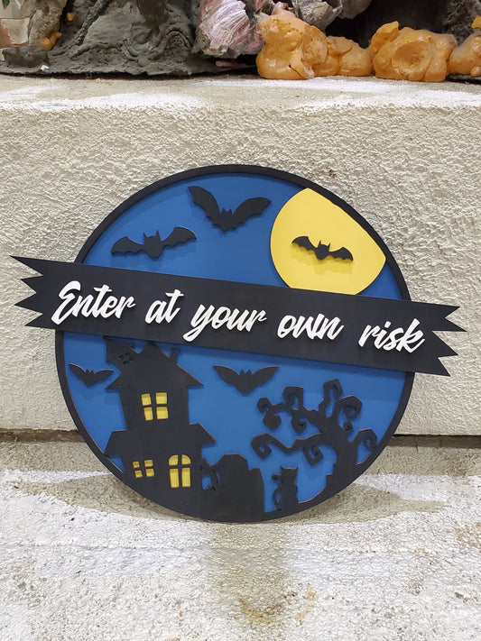 Halloween-themed decorative sign with bats, a moon, and a haunted house on a blue background. "Enter at your own risk". Door Round