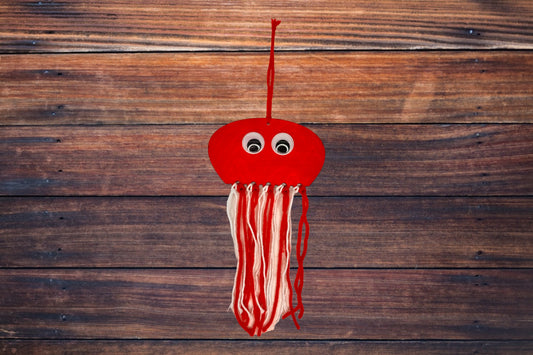 Laser cut wooden octopus hand painted red with wiggly eyes and red and white yarn ready to hang.