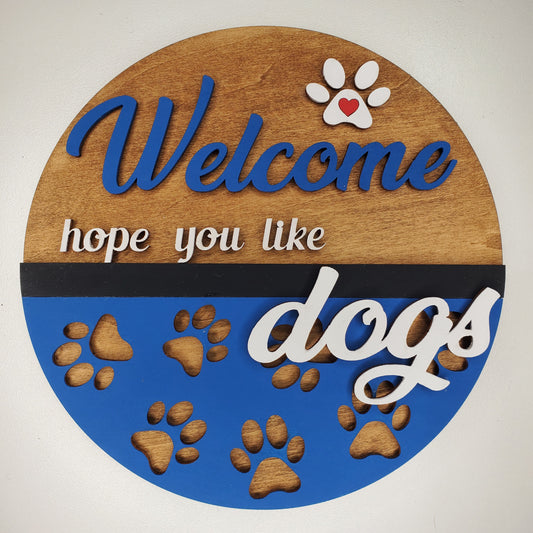 Laser cut wood door round, sign, featuring "Welcome Hope You Like Dogs"  with paw prints. Hand Painted blue and stain with white, black and red accents