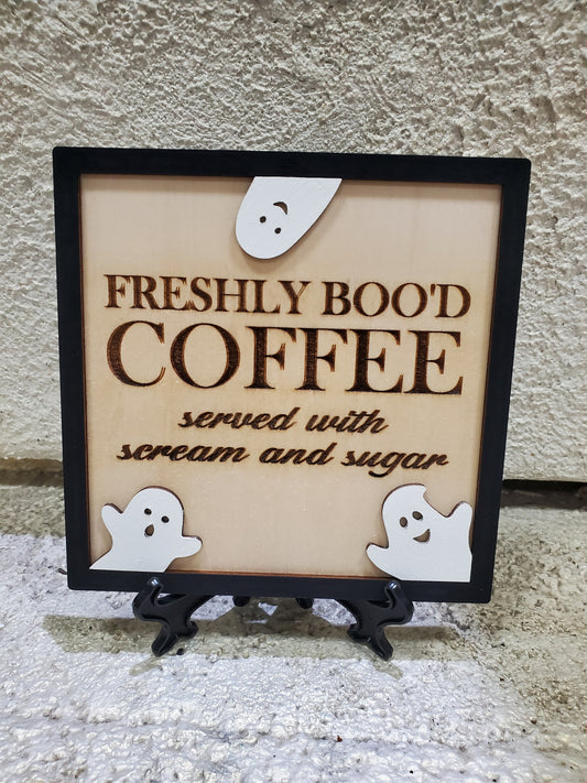 Decorative sign with 'Freshly Bood Coffee' text and ghost illustrations on a stand.