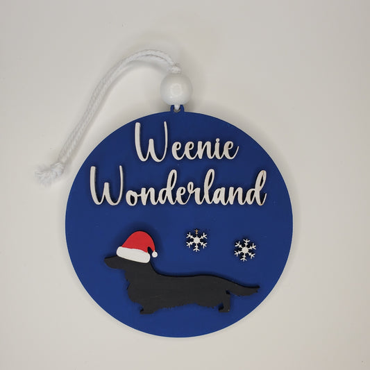 Decorative round ornament with 'Weenie Wonderland' text, dachshund silhouette, and snowflakes on a blue background. Wired, Smooth, and Long haired dogs available. Pick breed, dog color, and background color from available choices.