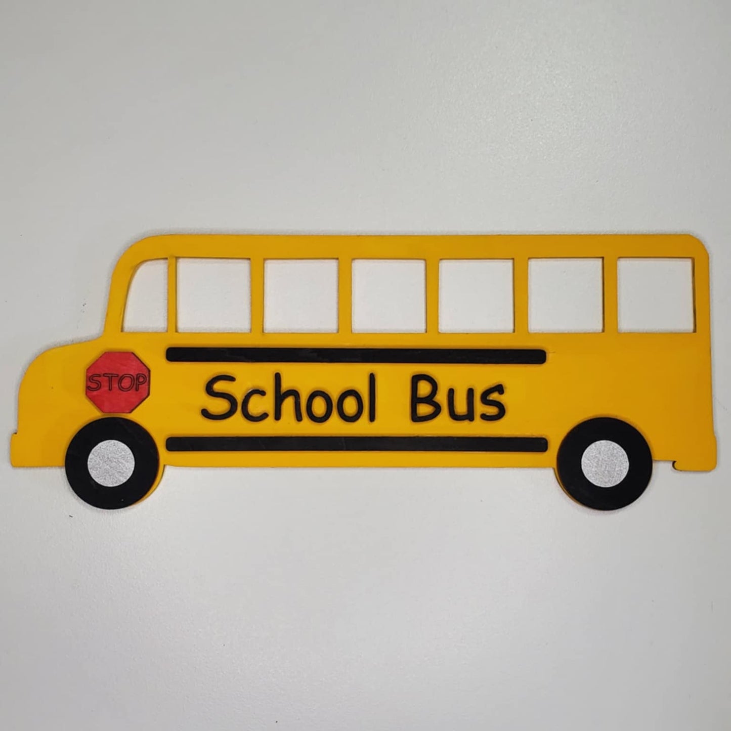 A laser cut wood school bus hand painted yellow with black and red stop sign.