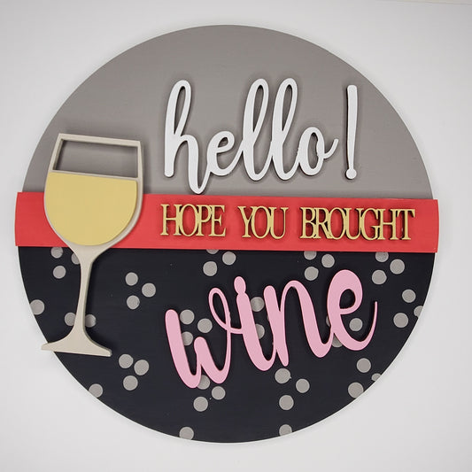 Decorative sign with a wine glass and text 'hello! Hope you brought wine' on a gray and black background. Door round or shelf leaner. Sizes 7inch, 12 inch or 16 inch. DIY kit available.