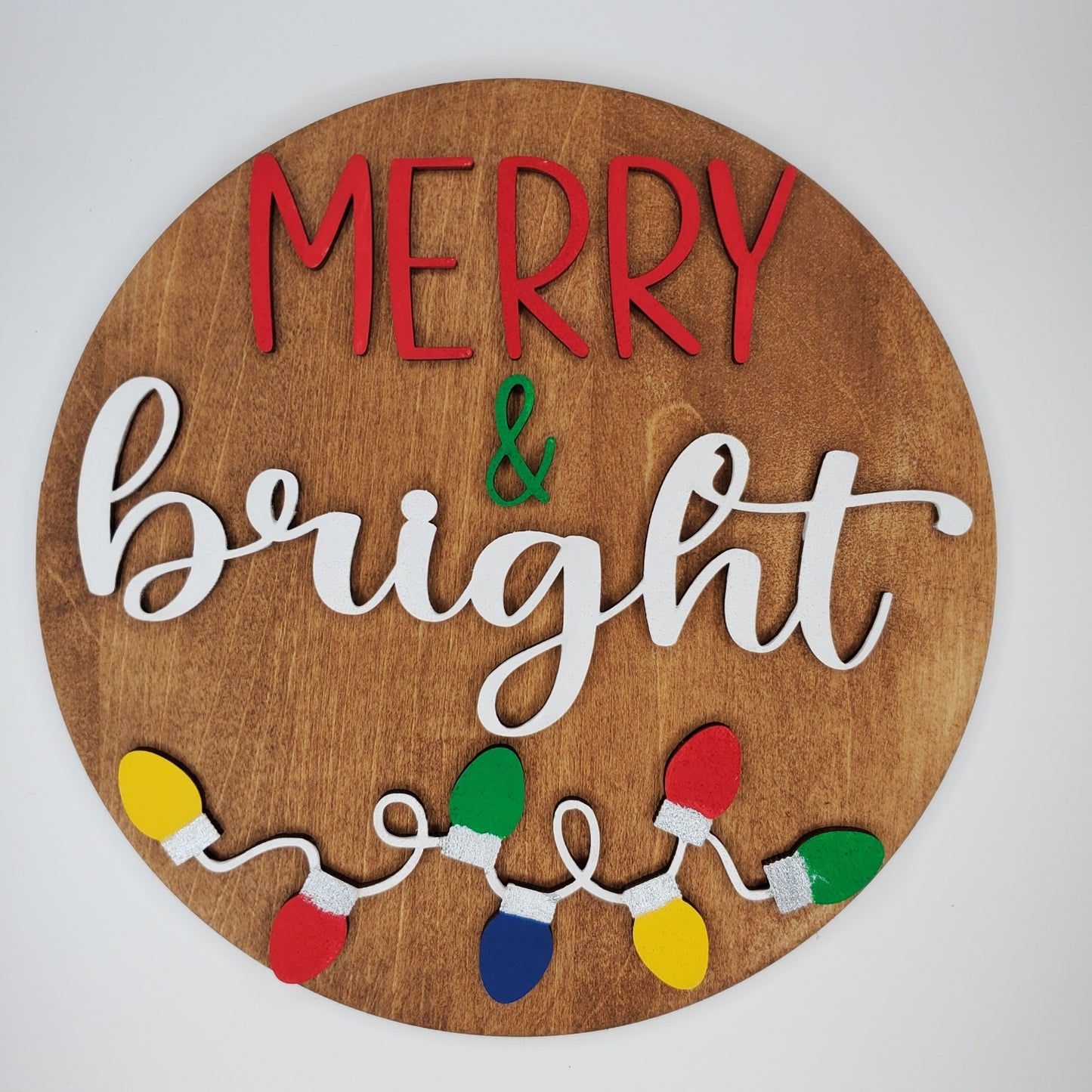 Wooden circular sign with 'Merry & Bright' text and Christmas lights on a brown background. Door round or shelf leaner. Sizes 7inch, 12 inch or 16 inch. DIY kit available.
