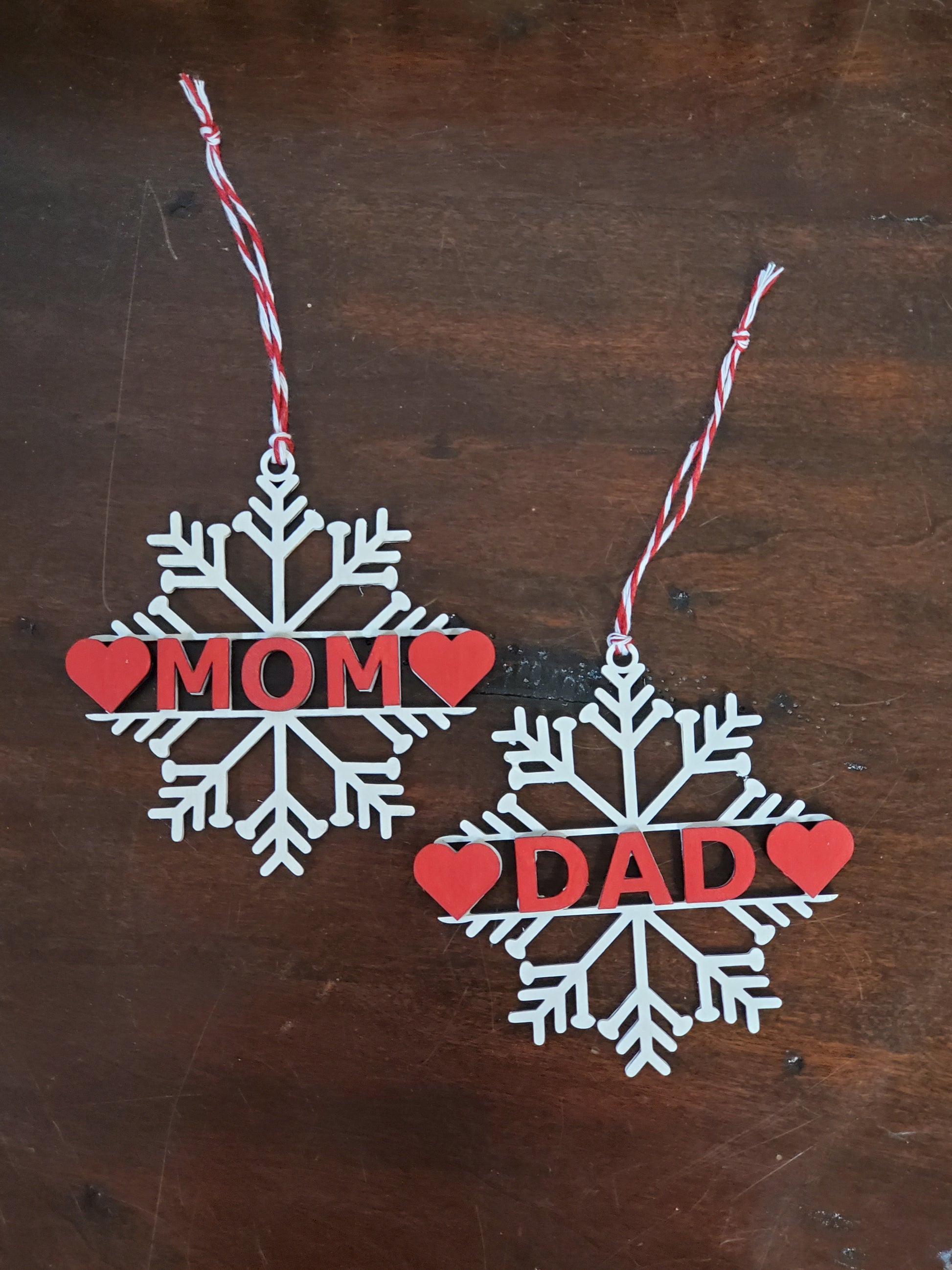 Two snowflake-shaped ornaments with 'Mom' and 'Dad' text on a wooden surface